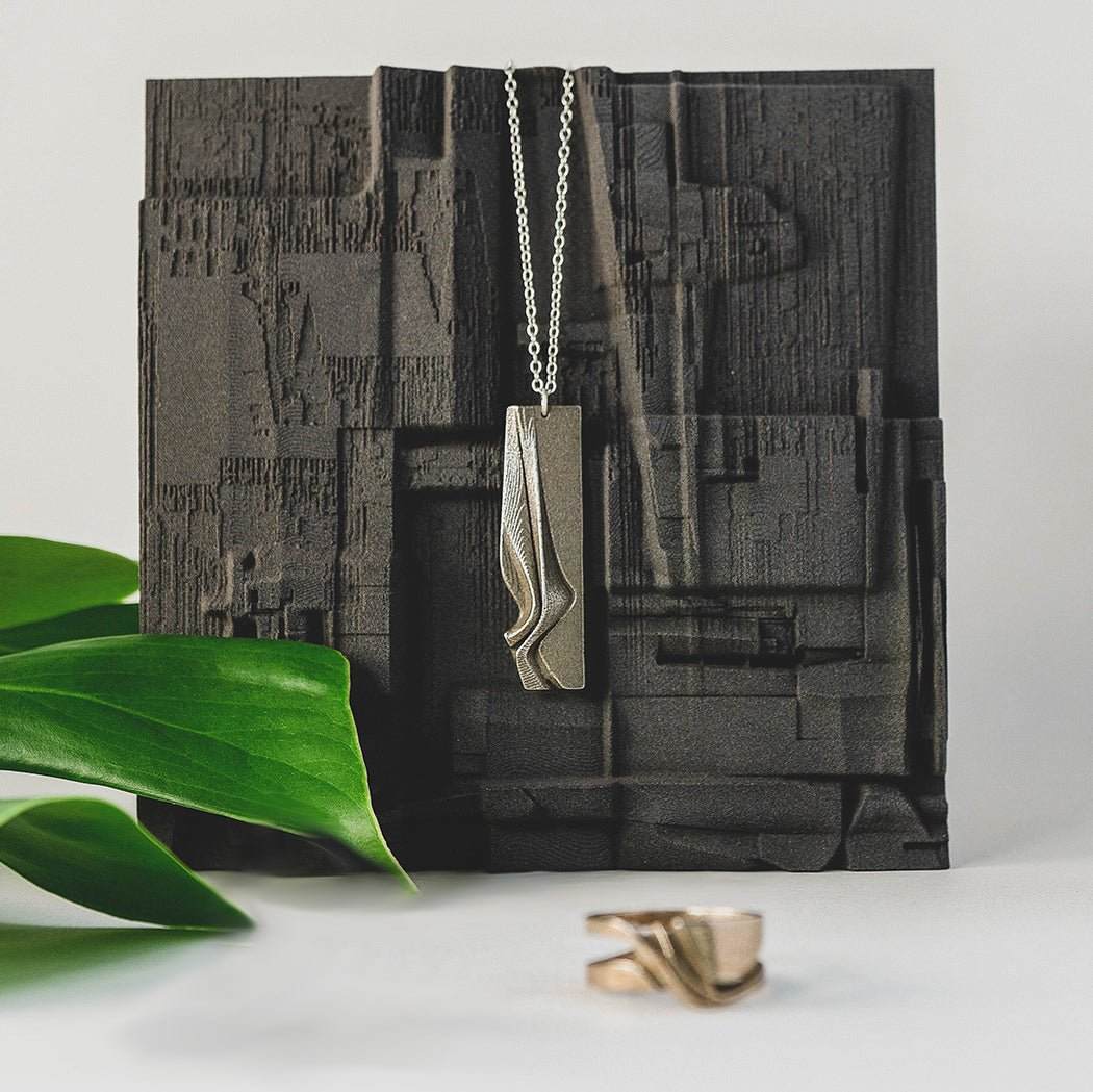 Nocturne Velum Gift Set featuring Gray Steel pendant with rippling curves and a matching ring displayed on textured black background with green leaf