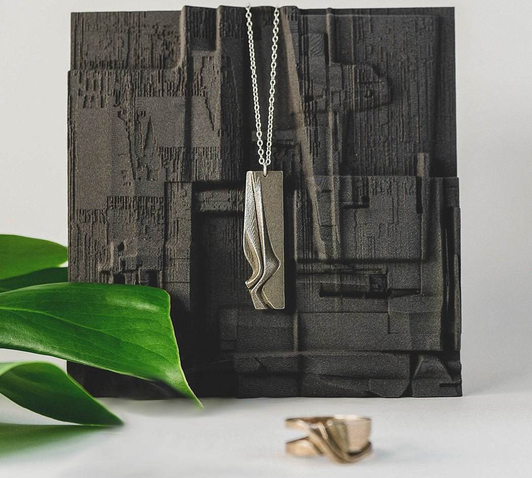 Nocturne Velum Gift Set featuring Gray Steel pendant with rippling curves and a matching ring displayed on textured black background with green leaf