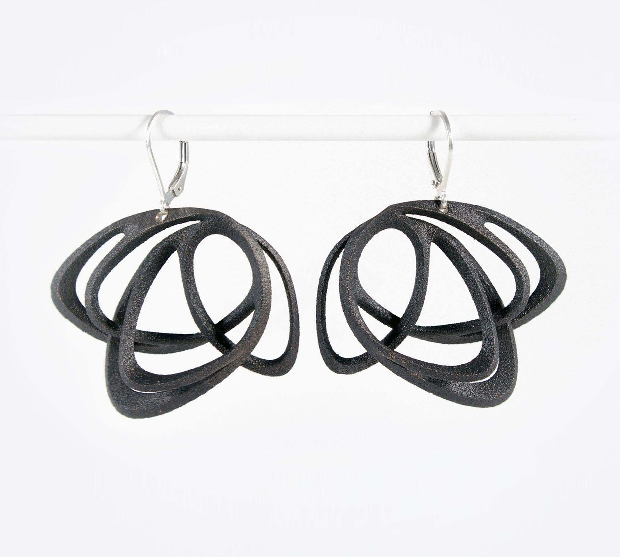 Pair of black steel Gemino earrings with interlocking elliptical petals design hanging on a white rod